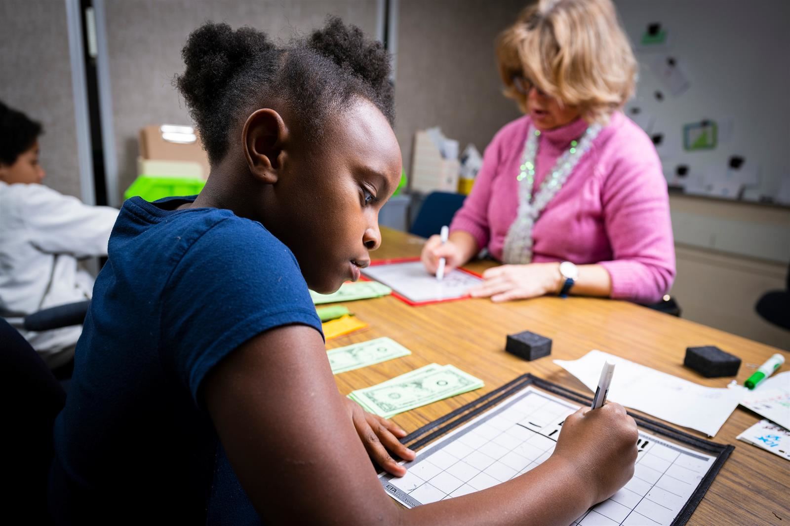 Student doing school work on a desk with her teacher nearby